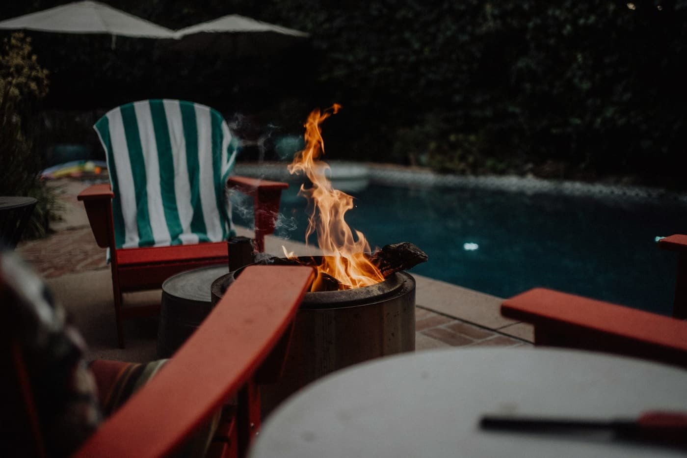 Lit fire bowl beside chairs with a glowing pool behind